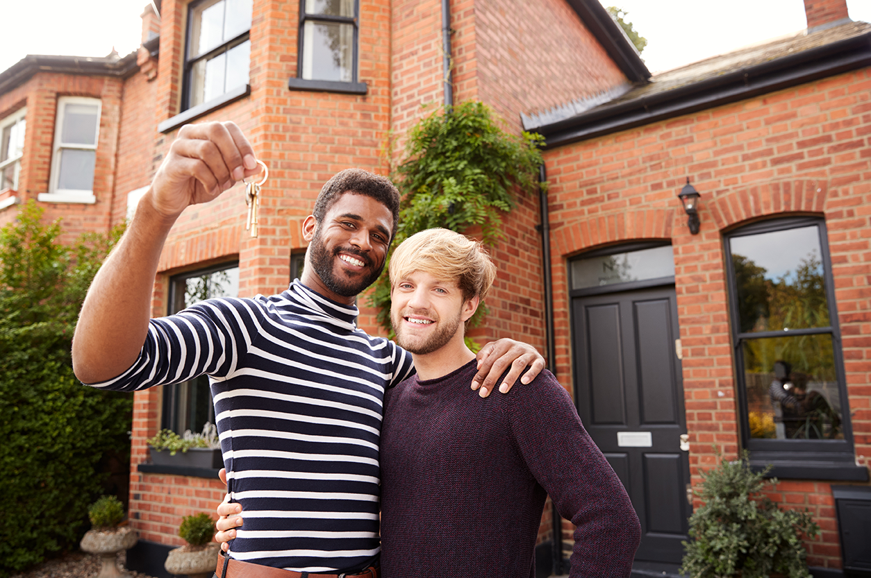 Image of a same sex couple standing in front of their new home holding up keys