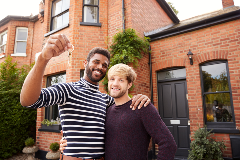 Image of a same sex couple standing in front of their new home holding up keys