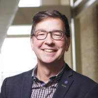 David Christianson headshot. He is wearing a plaid shirt, dark blue blazer and has glasses