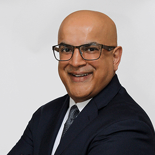 Iftikhar Mahmood headshot. He is smiling widely with arms crossed confidently. He is wearing a dark blue suit and has glasses