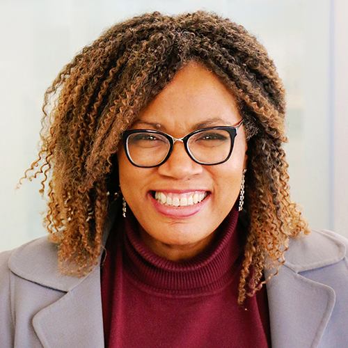 Jackie Porter headshot. She is wearing a dark red turtleneck with a light grey jacket, and has glasses