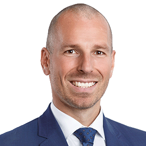 Ryan Gubic headshot. He is smiling at the camera and is wearing a blue suit and blue tie.